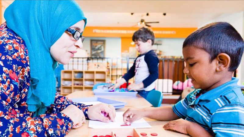 A teacher in a headscarf plays a counting game with a young boy