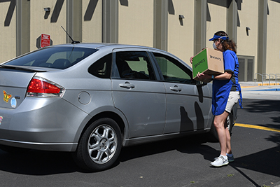 An MJC employee holding a box speaks to a student through their car window.