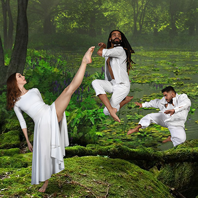 Three dancers clad in white appear to float in the air as they contort their bodies in remarkable ways before a backdrop of a magical forest.